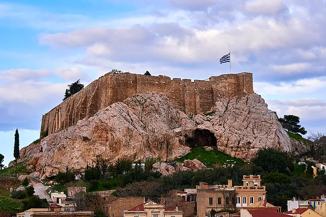The Acropolis rock with its walls and a Greek flag rising above the old rooftops of Plaka