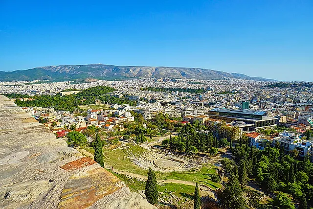 View from the Acropolis wall over the Theatre of Dionysus and the green slope, with Athens stretching to the mountains